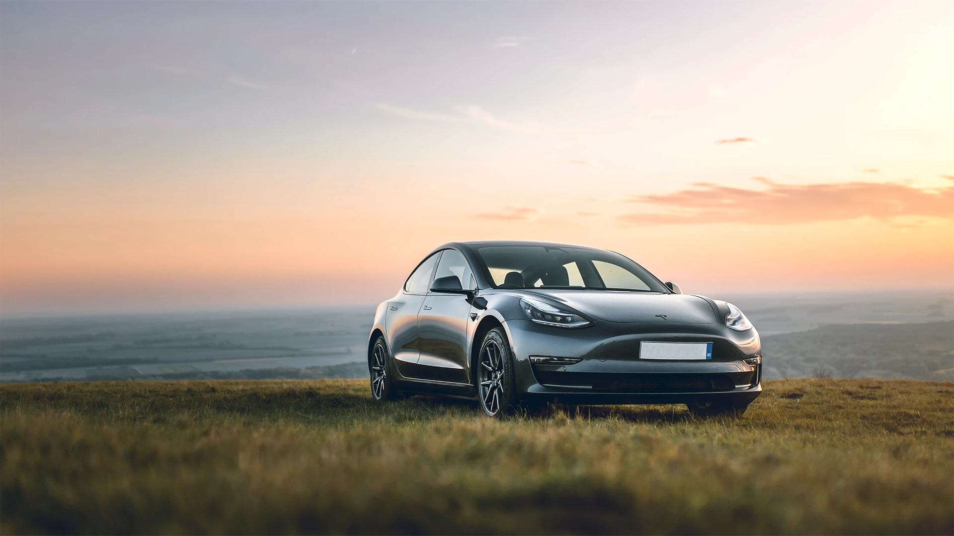 Grey Tesla in a field with sunrise